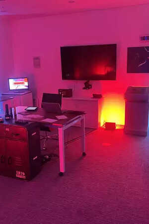 Fully themed escape room for Brit Insurance featuring a dimly lit room with red and blue lights, a desk, computer, and a TV.